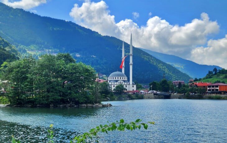 uzungöl cami manzarası ve göl kıyısından görünen yeşil dağlar eşliğinde yaz günü uzungöl panoraması
